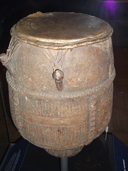 A wooden drum is on display in a glass case.