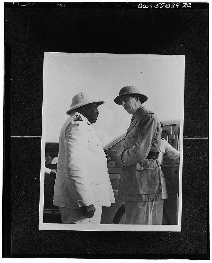 Two men in military uniforms standing next to a car.